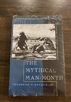 A shrink-wrapped copy of The Mythical Man-Month by Frederick P. Brooks, Jr., on a wooden table
