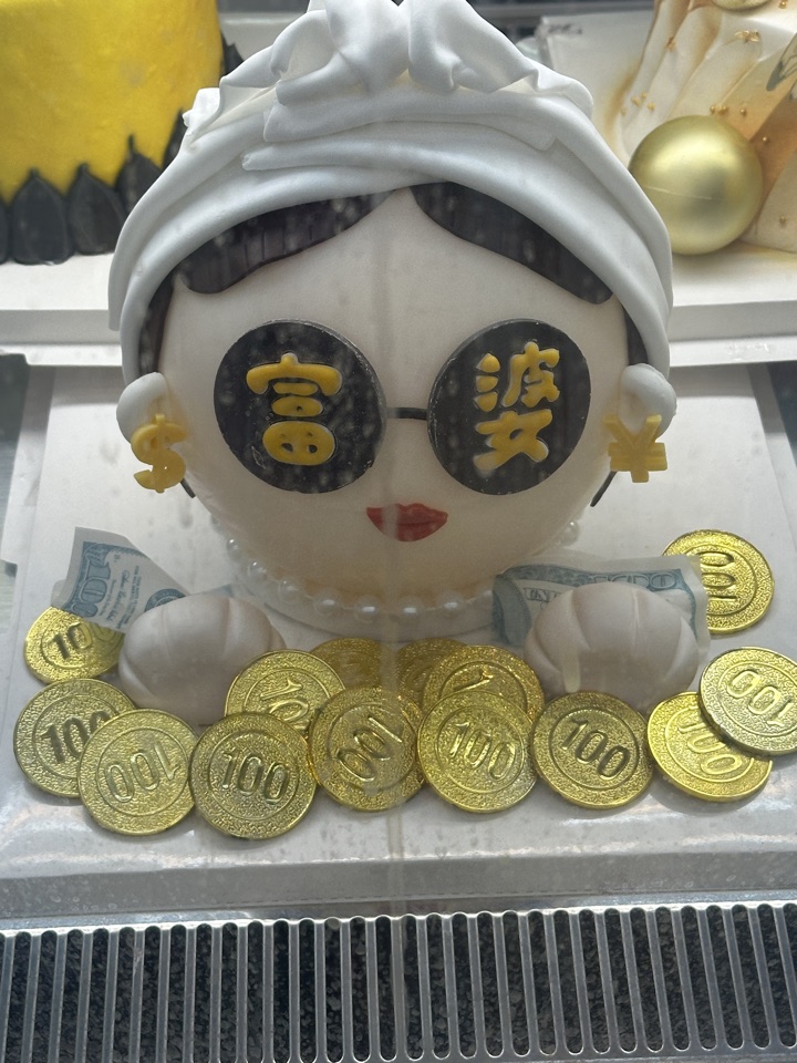 A cake shaped like a woman in sunglasses, surrounded by gold chocolate coins and banknotes